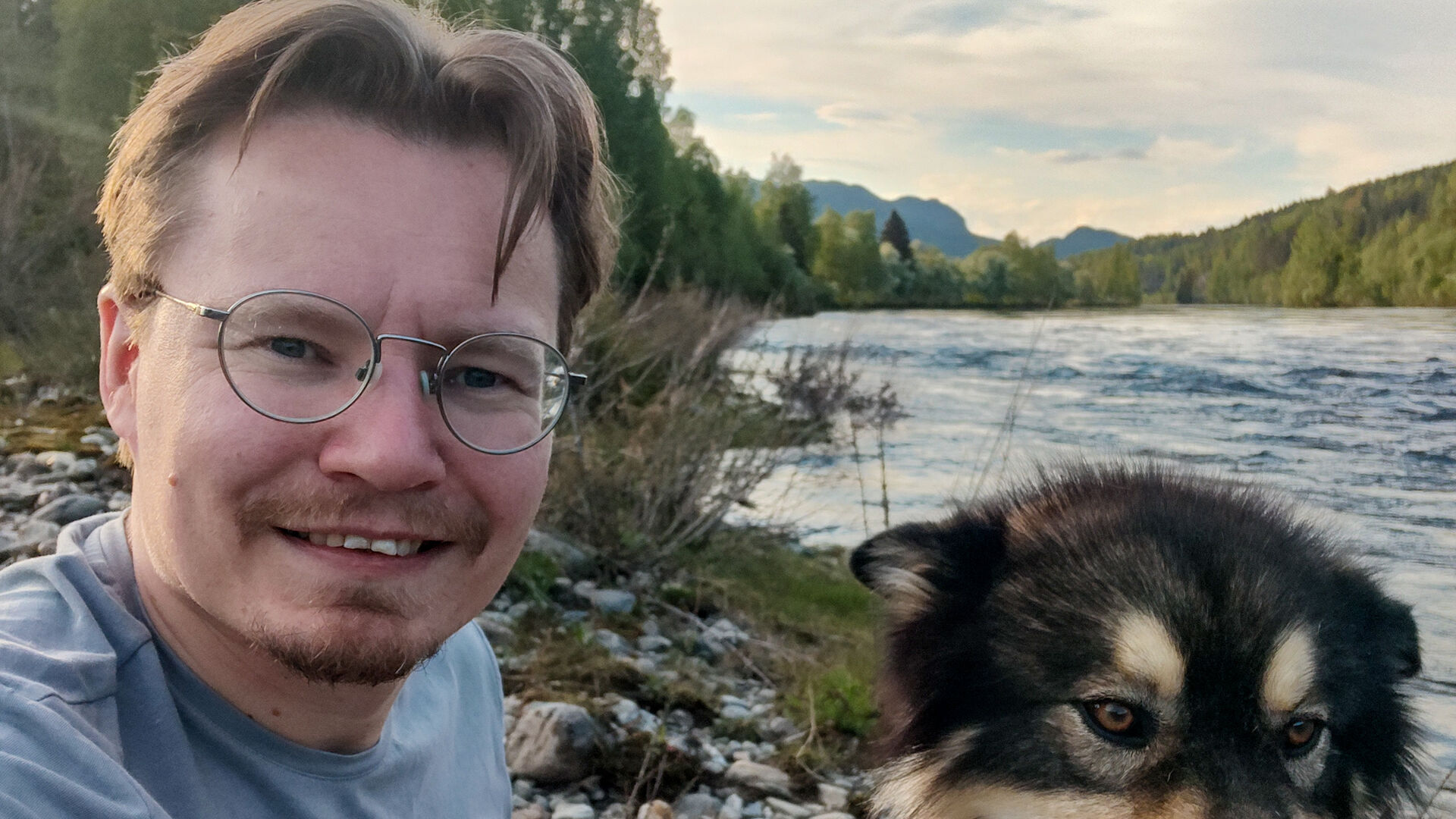 Mann med briller ute ved en elv sammen med en hund