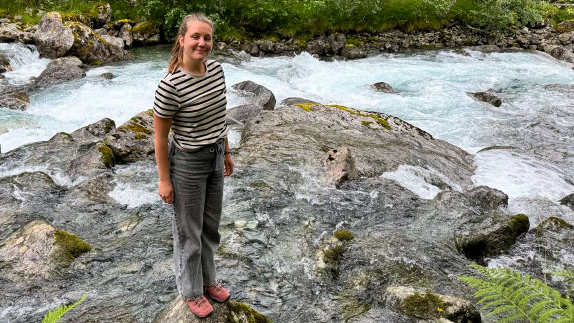Ung dame med stripete genser står ved en elv