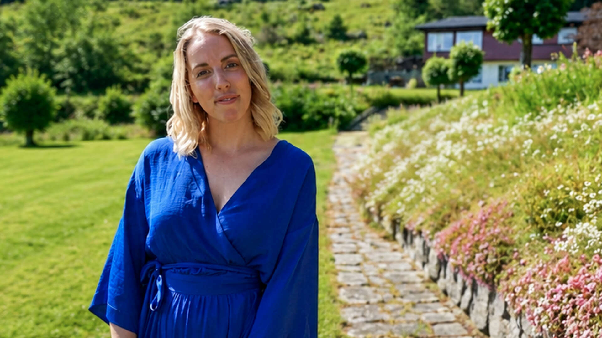 Dame med blå bluse på en plen foran et blomsterbed