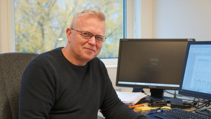 Bilde av Per Kristian ved PC-en foran et vindu med høstgult tre utenfor