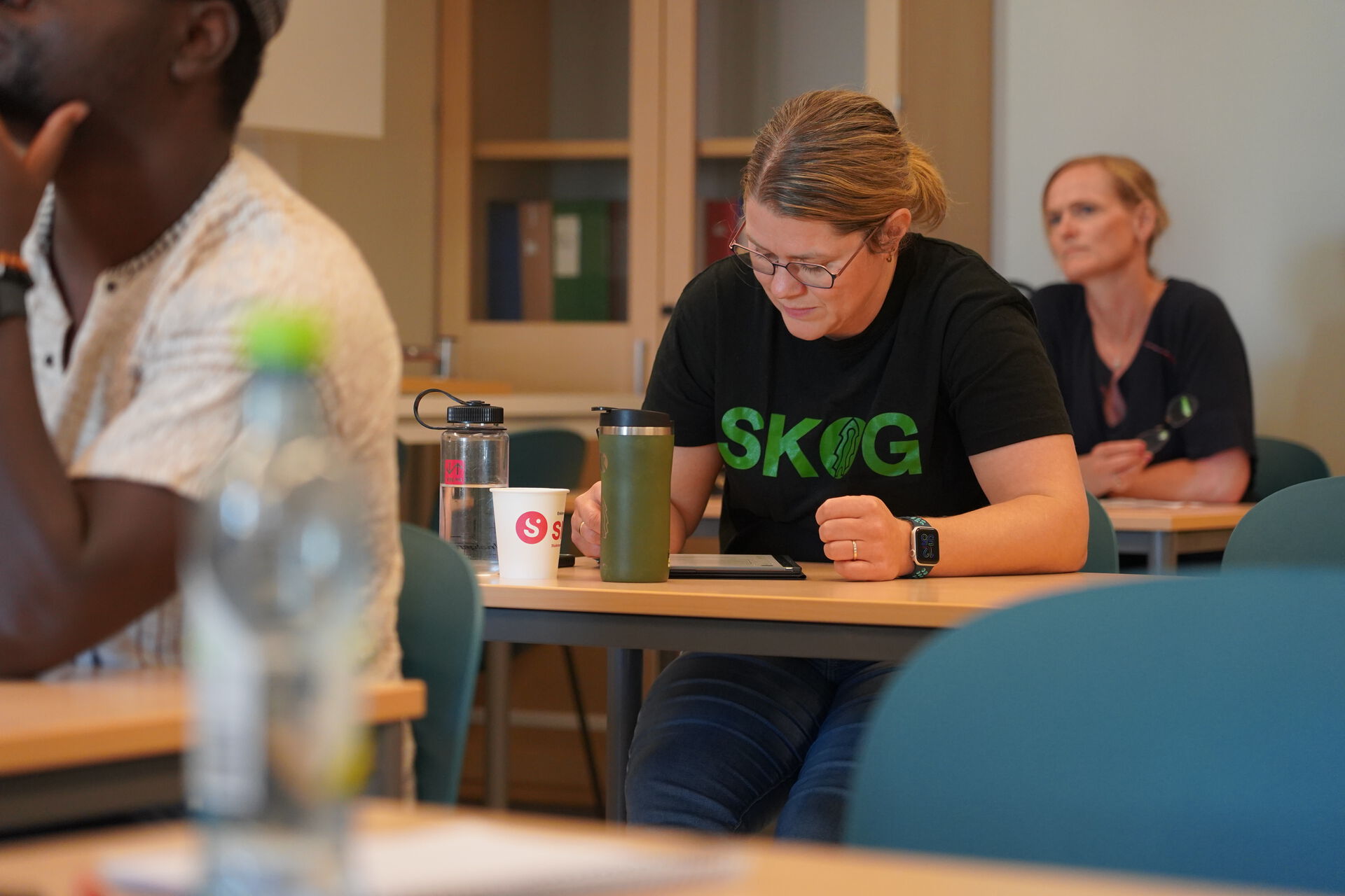 Dame med teksten SKOG på t-skjorta skriver ved en pult