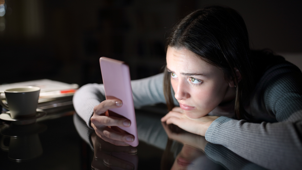 Jente i mørket som lyses opp av mobilen hun ser på
