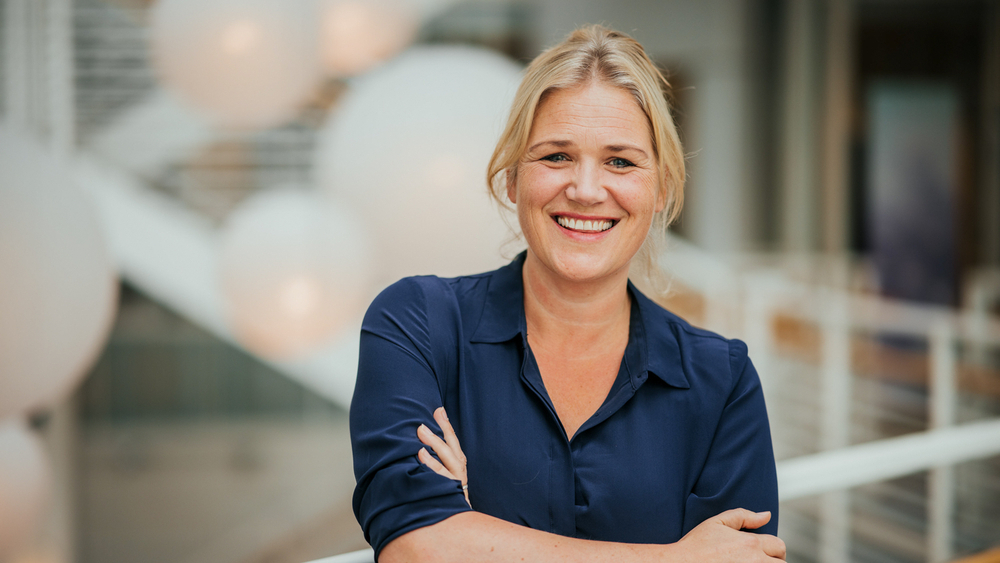 Portrettbilde av Camilla Bakken Øvald mot noen hvite, runde store taklamper og et gelender