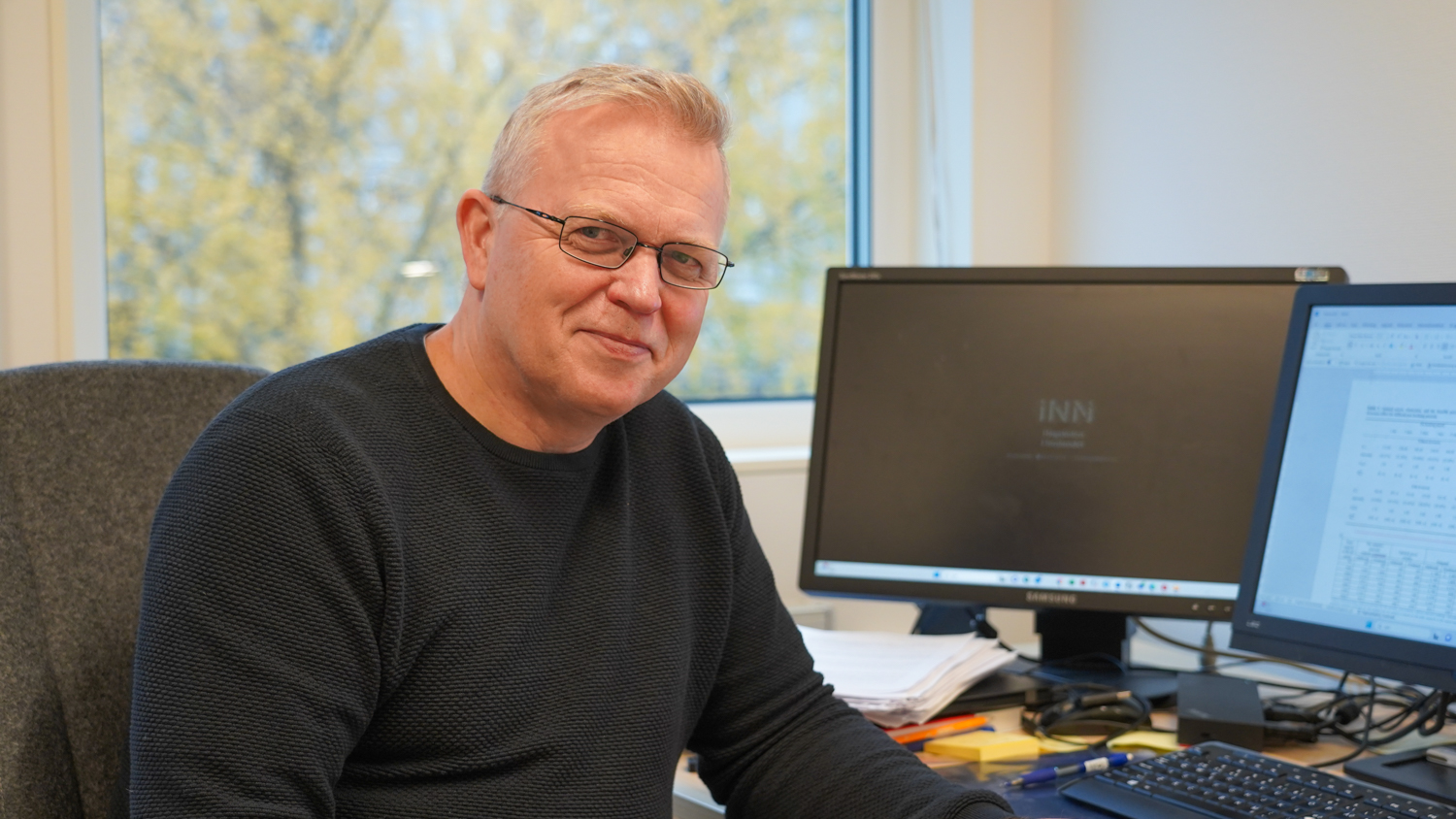Portrettbidle av Per Kristian foran PC med et vindu i bakgrunnen der du kan se et høstgult tre utenfor