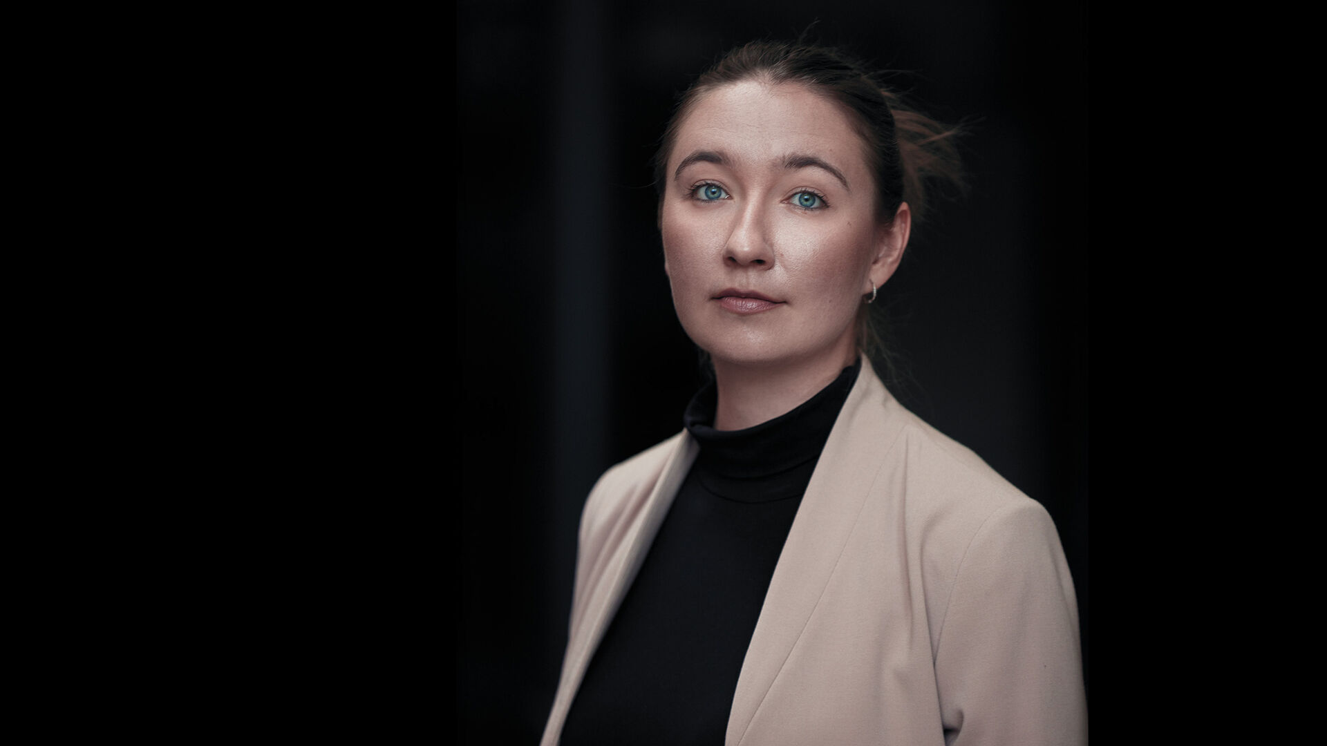 PPortrettbilde av ung dame med beige jakke, svart genser mot svart bakgrunn
