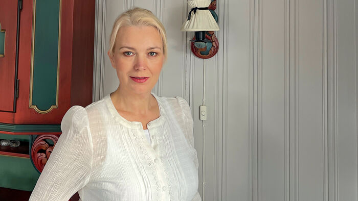 Dame med hvit bluse foran en hvit vegg og et gammel skap