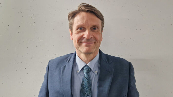 POrtrettbilde av mann med blå jakke og slips mot en hvit vegg