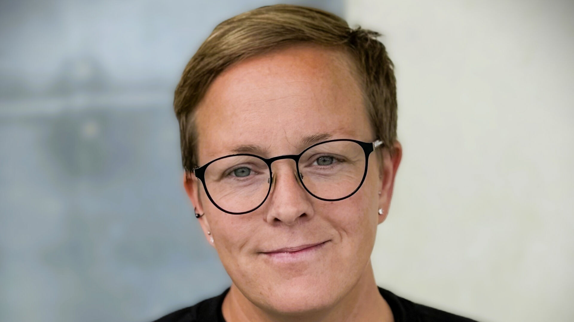 Dame med kort hår og briller mot uskarp bakgrunn