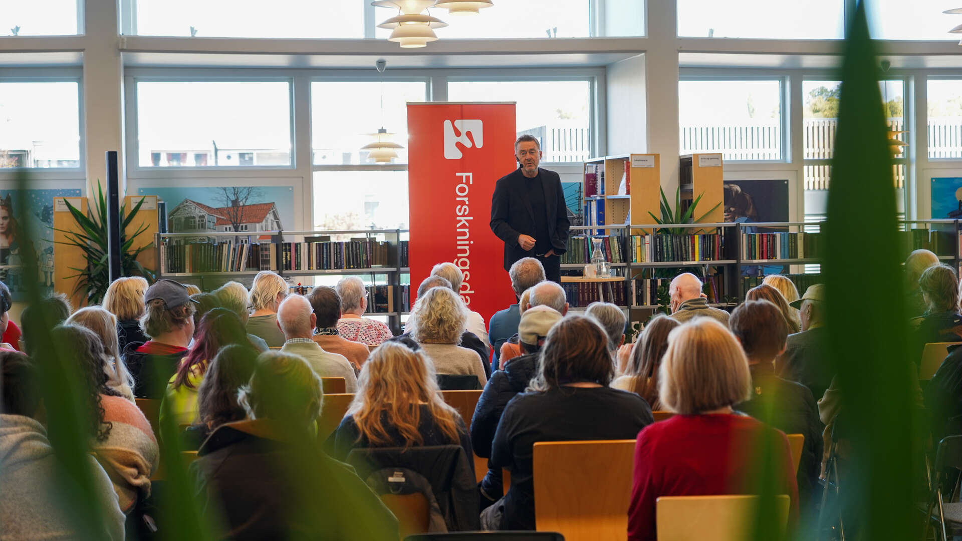 Mann på en scene holder foredrag foran publikum på et bibliotek