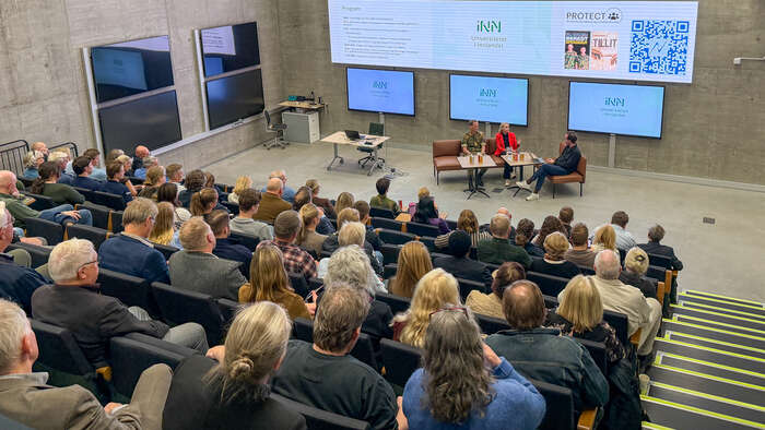 En fullsatt sal hører på en samtale mellom tre personer foran dem