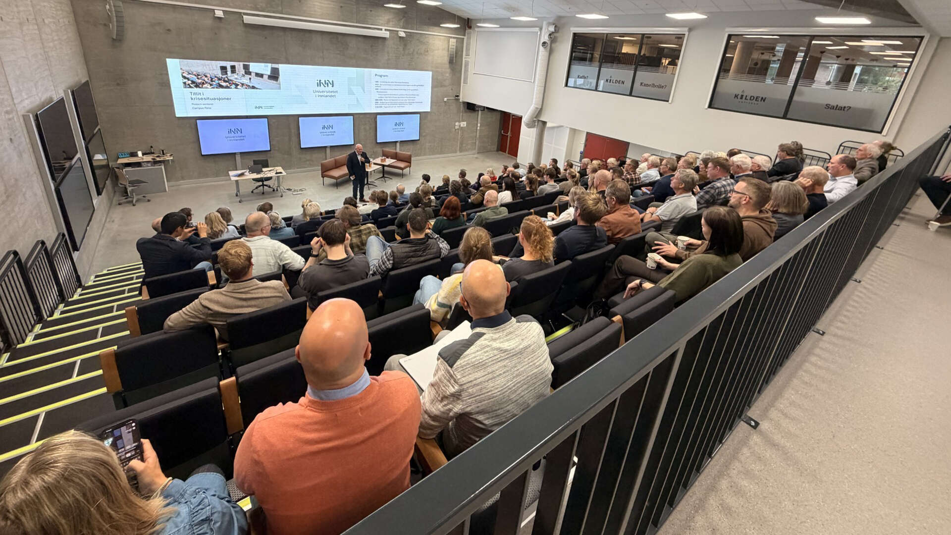 Mann står foran et fullsatt auditorium i et murrom