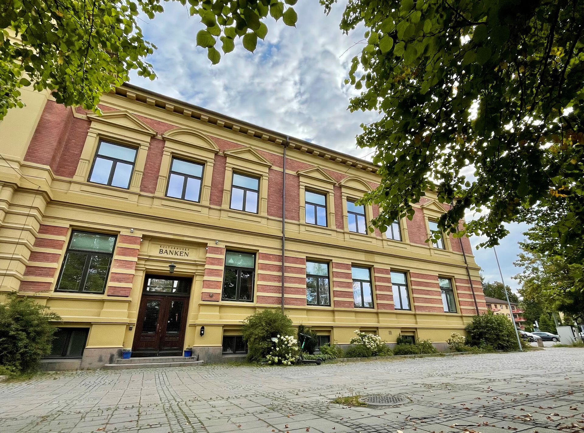 Bilde av Kulturhuset Banken i Lillehammer utenfra med grønne trær i forkant