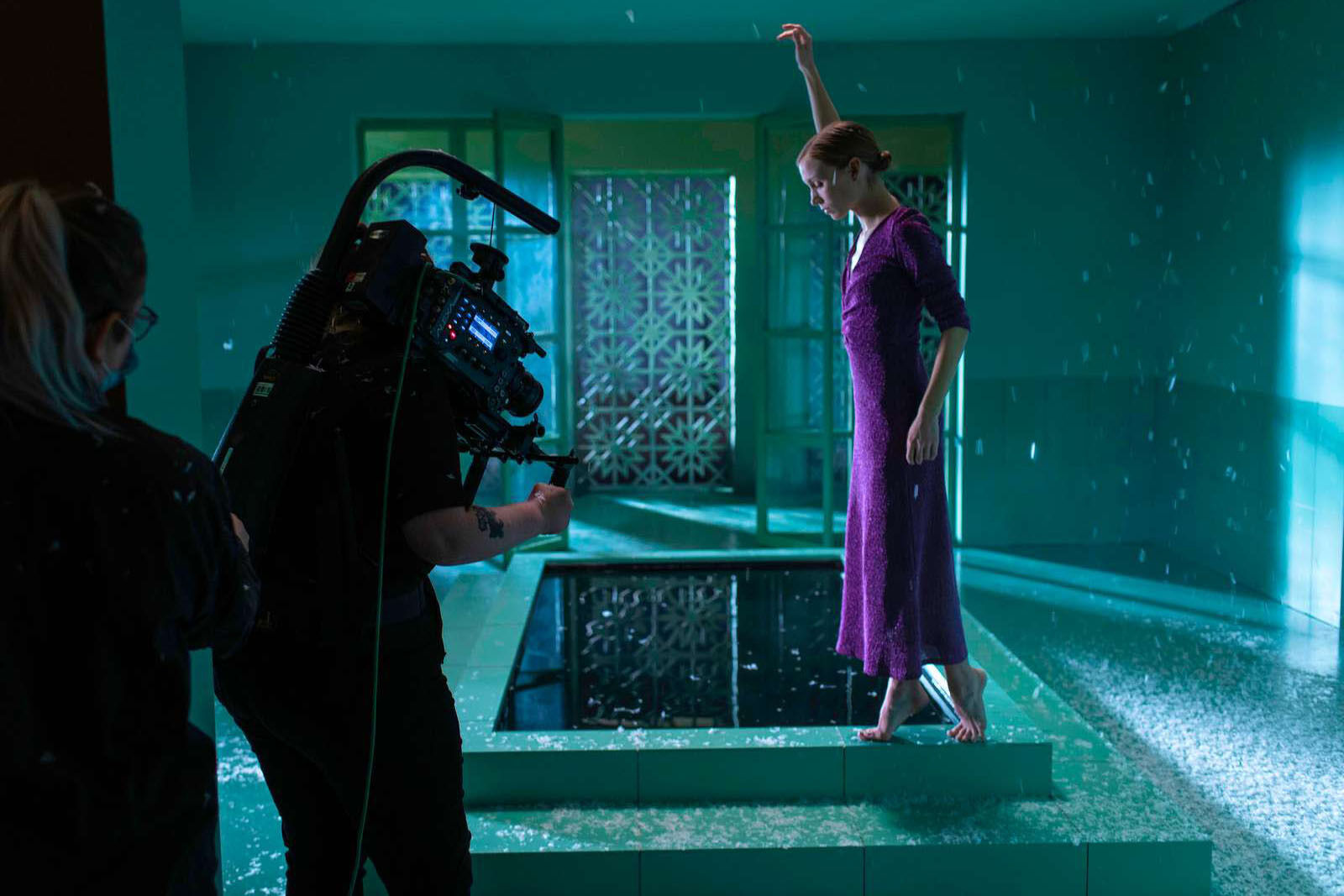 Dame i lilla kjole balanserer på kanten av basseng mens hun blir filmet.