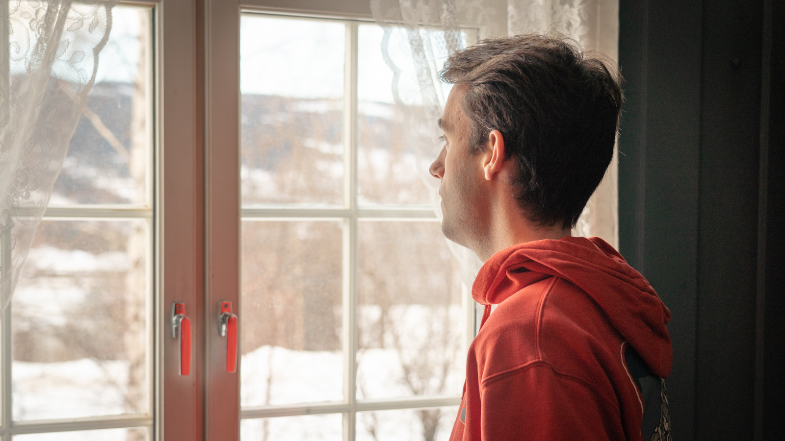Stian in profile from the left. He is wearing a red hoodie and is looking out the window