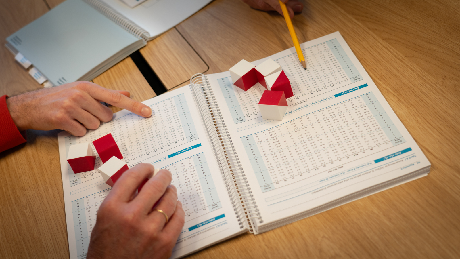Hands touching red and white building blocks over a book full of numbers
