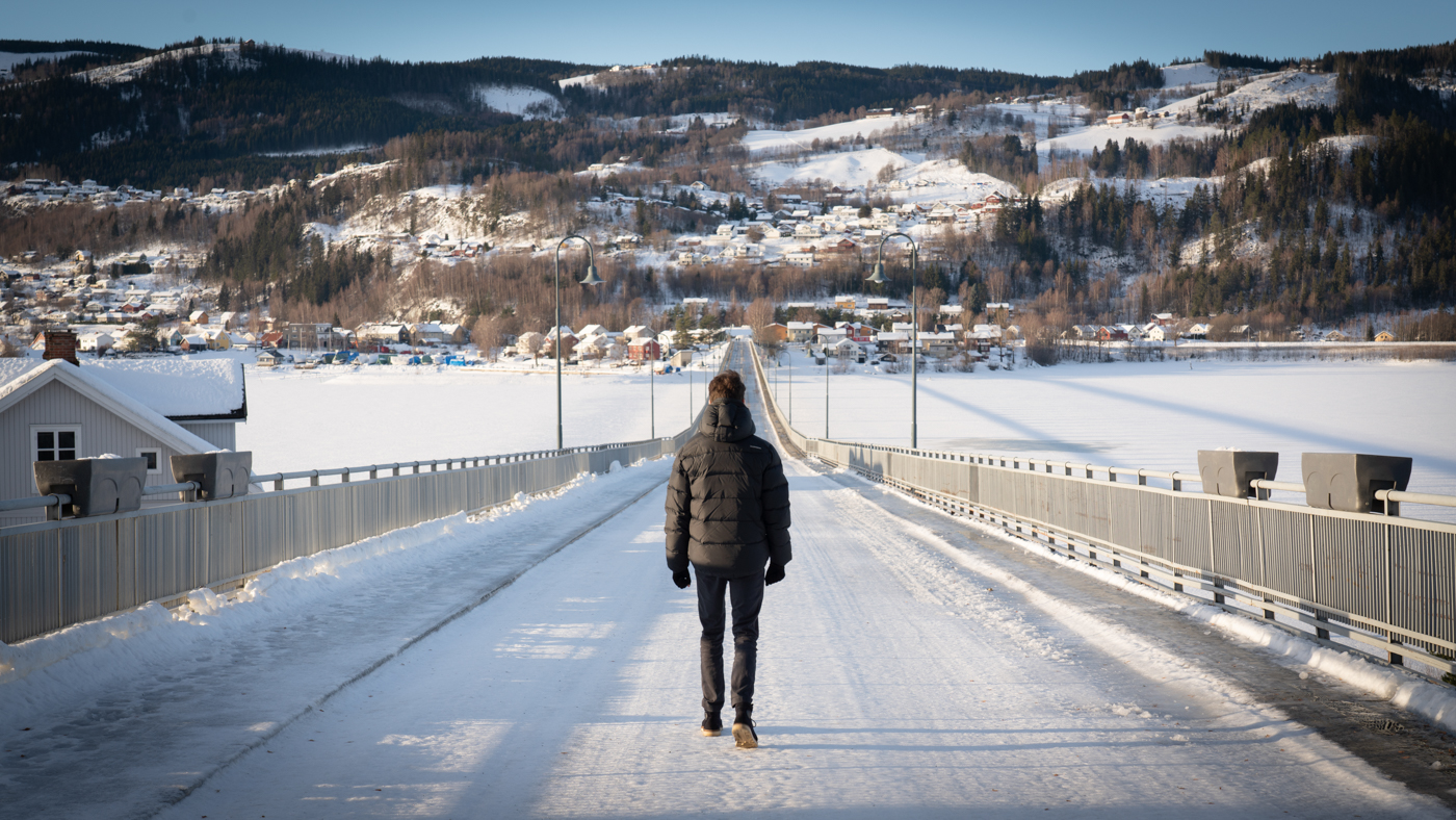 Stian med ryggen mot går over snødekt bro.
