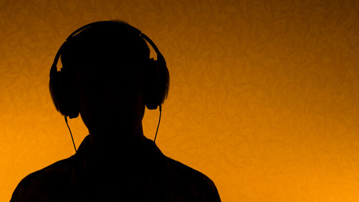 Siluett av en person som lytter til musikk med headset mot en oransje bakgrunn