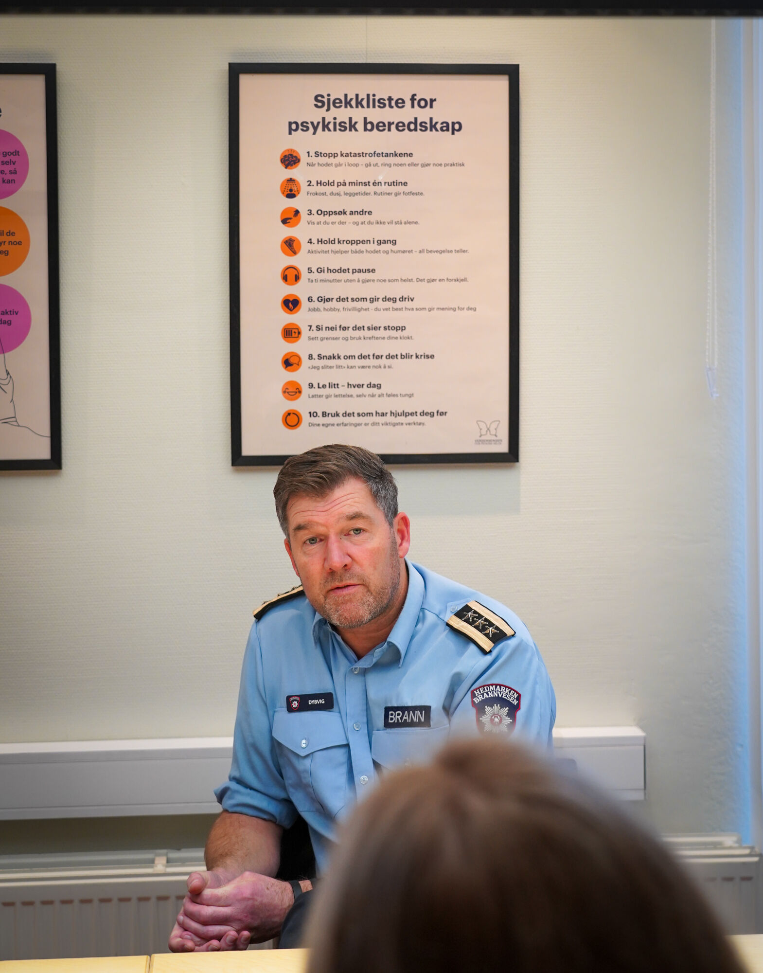 Brannmann sitter ved et bord med en plakat bak seg på veggen
