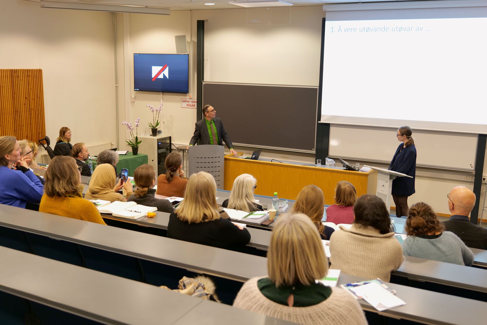 Andreopponent og doktorand i samtale med publikum i salen. 