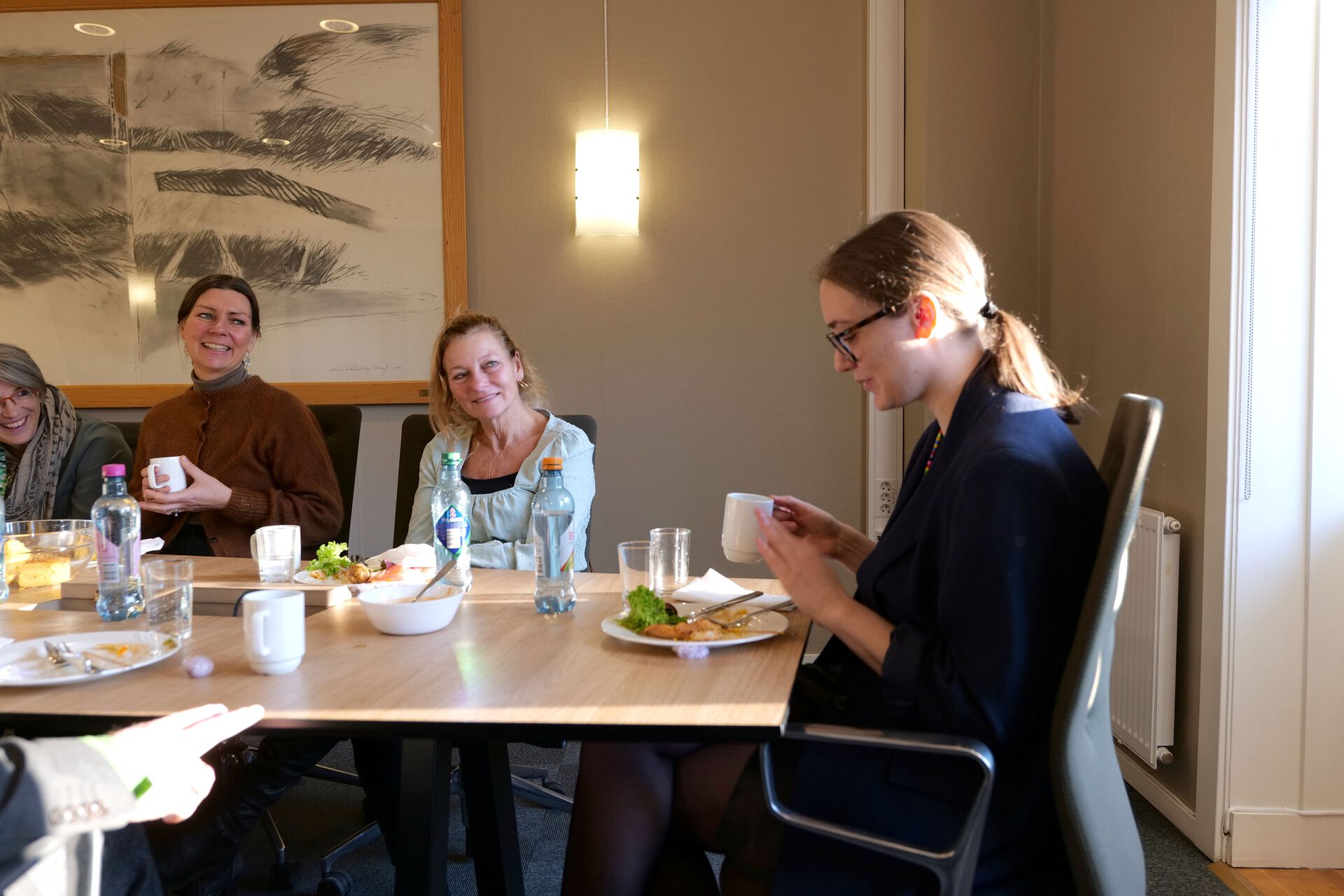 Mennesker sitter rundt et bord og spiser lunsj. Doktoranden sitter ved enden.n av bo