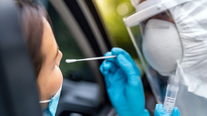 Person i medisinsk verneutstyr tar kovid-test i nesa til person i bil under pandemien