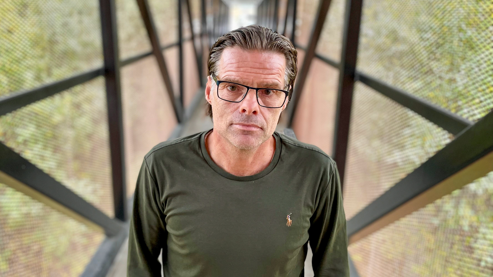 Forsker Christer Thrane i en utendørs gang med metallstolper i mønster mot et gjennomsiktig gitter