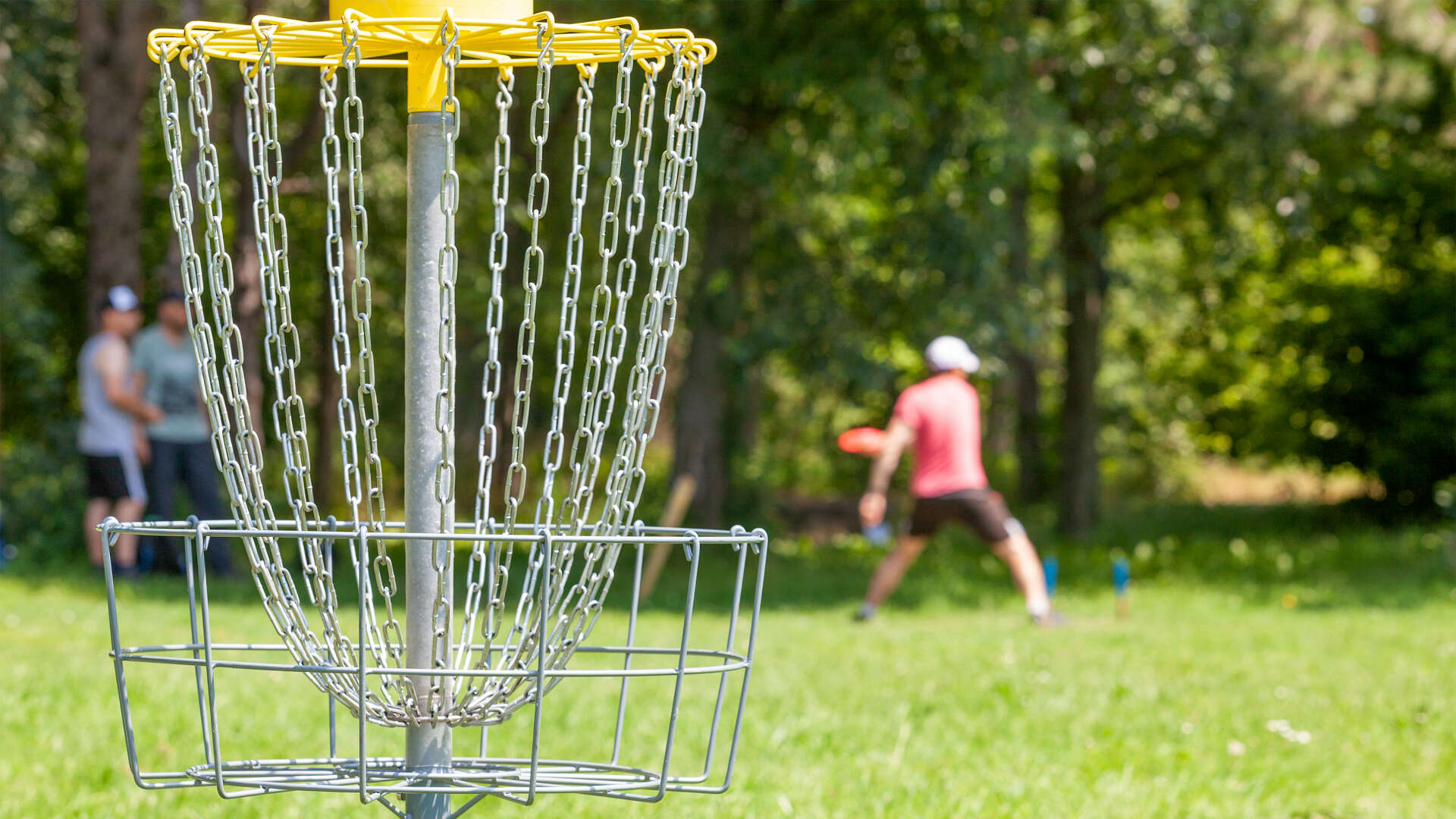En frisbeegolf-kurv med noen som kaster frisbee i bakgrunnen