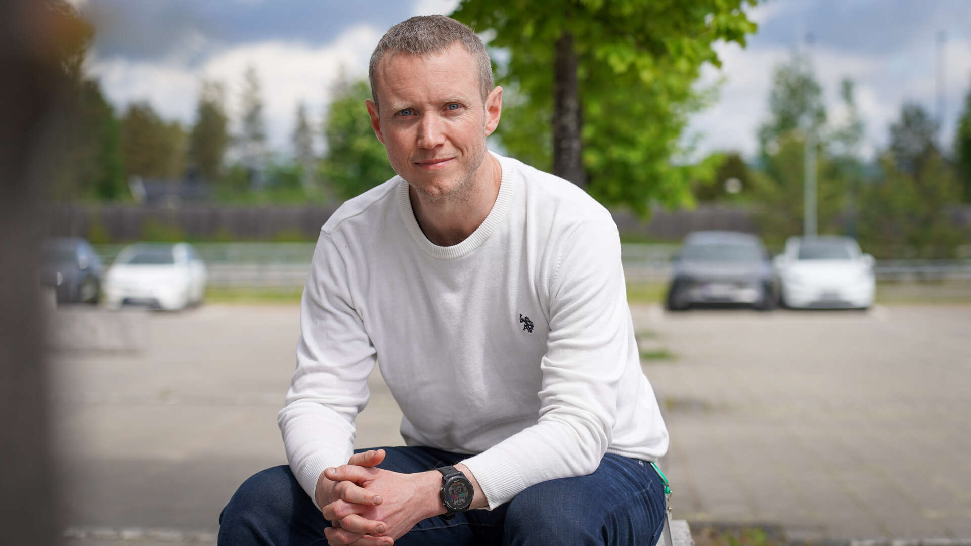 Mann med hvit genser sitter på en stor steinbenk på en parkeringsplass