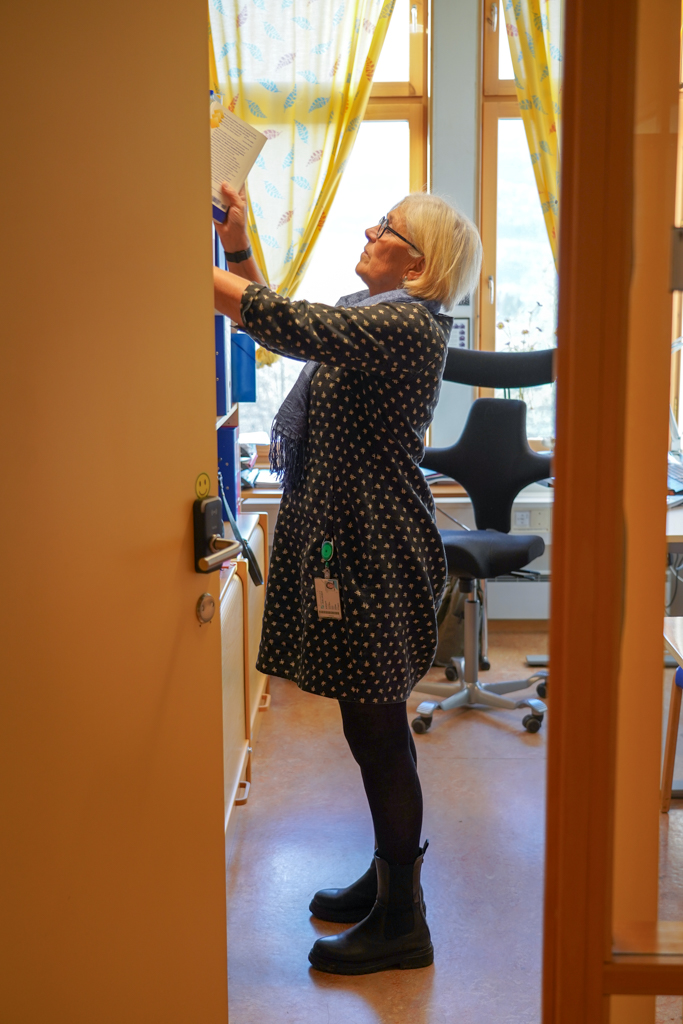 Anne Stine setter bok på på plass i bokhylle - bildet er tatt fra siden.