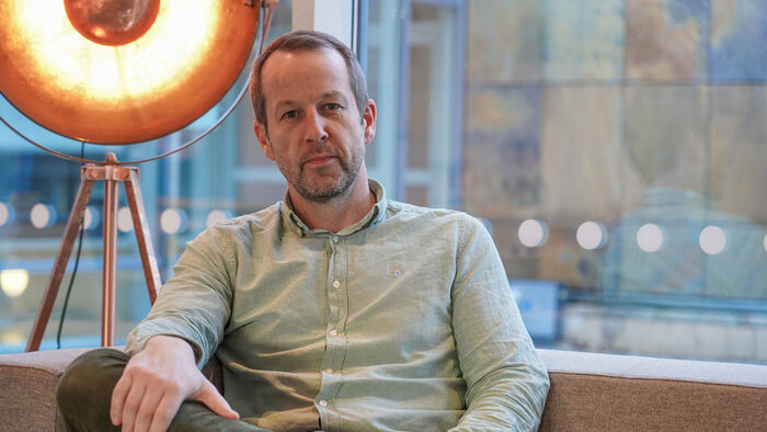 Lars Christie sitter i en sofa med en stor lampe bak seg og et stort vindu