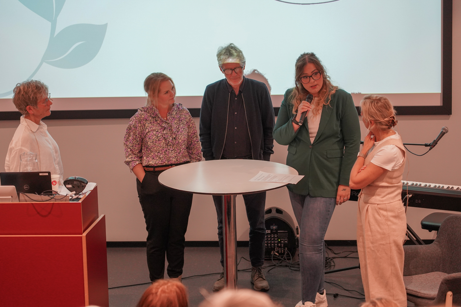 Et panel av folk foran lysbilde på hvit vegg
