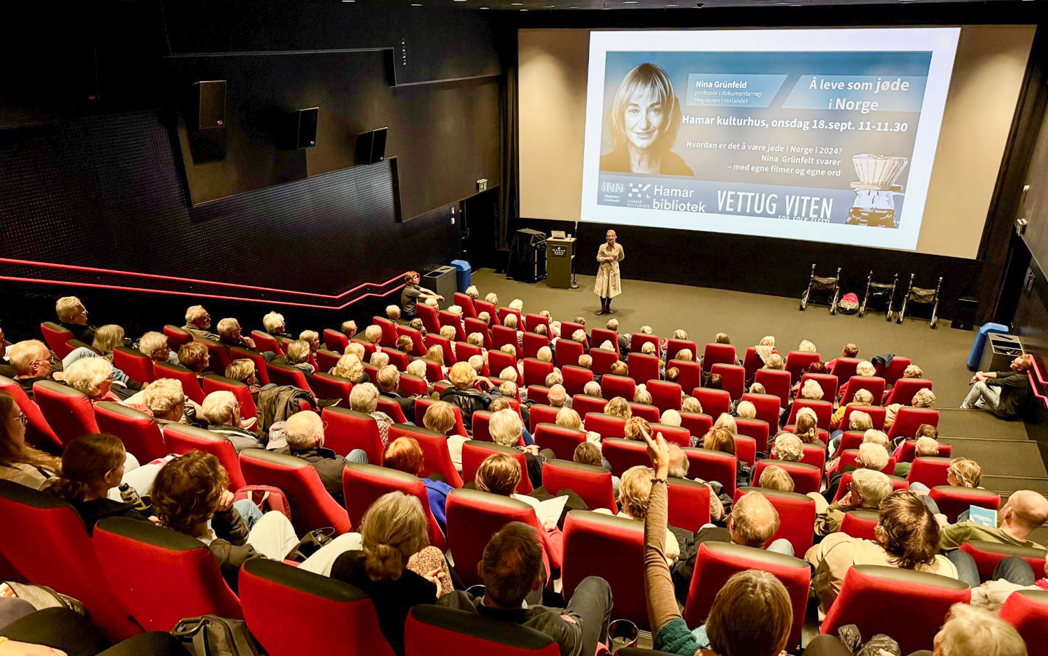 NIna Grünfeld foran en fullsatt kinosal med bilder på lerretet