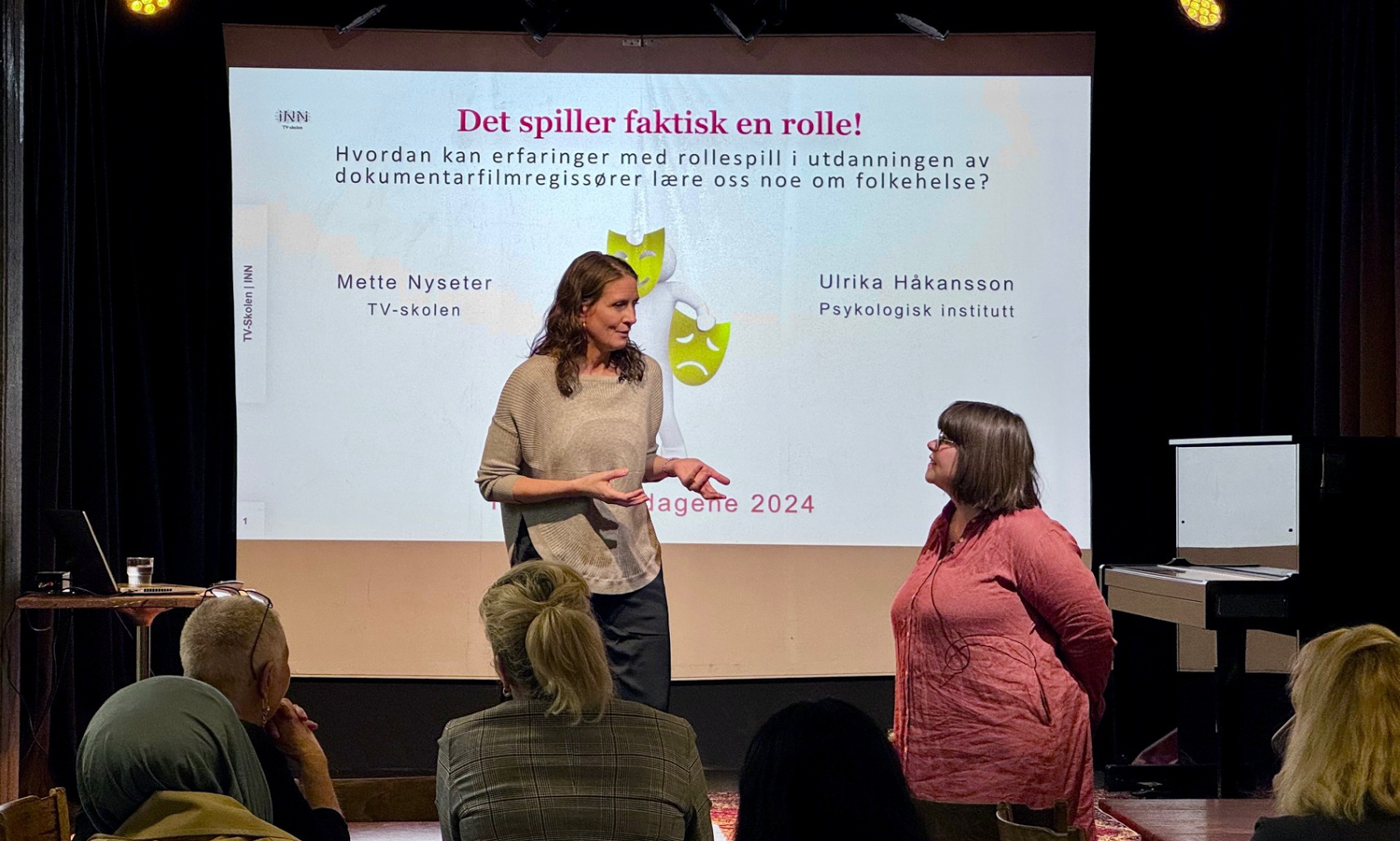 To damer på en scene med powerpointbilde på et lerret bak seg