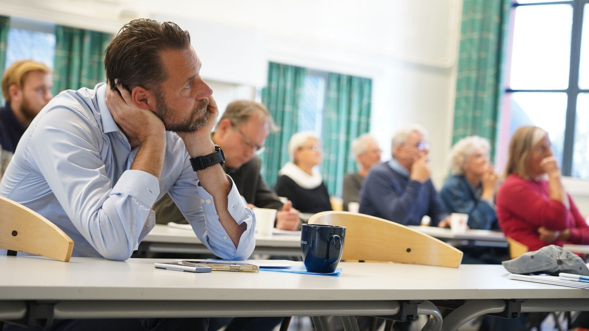 Voksne folk sitter ved pulter i et klasserom
