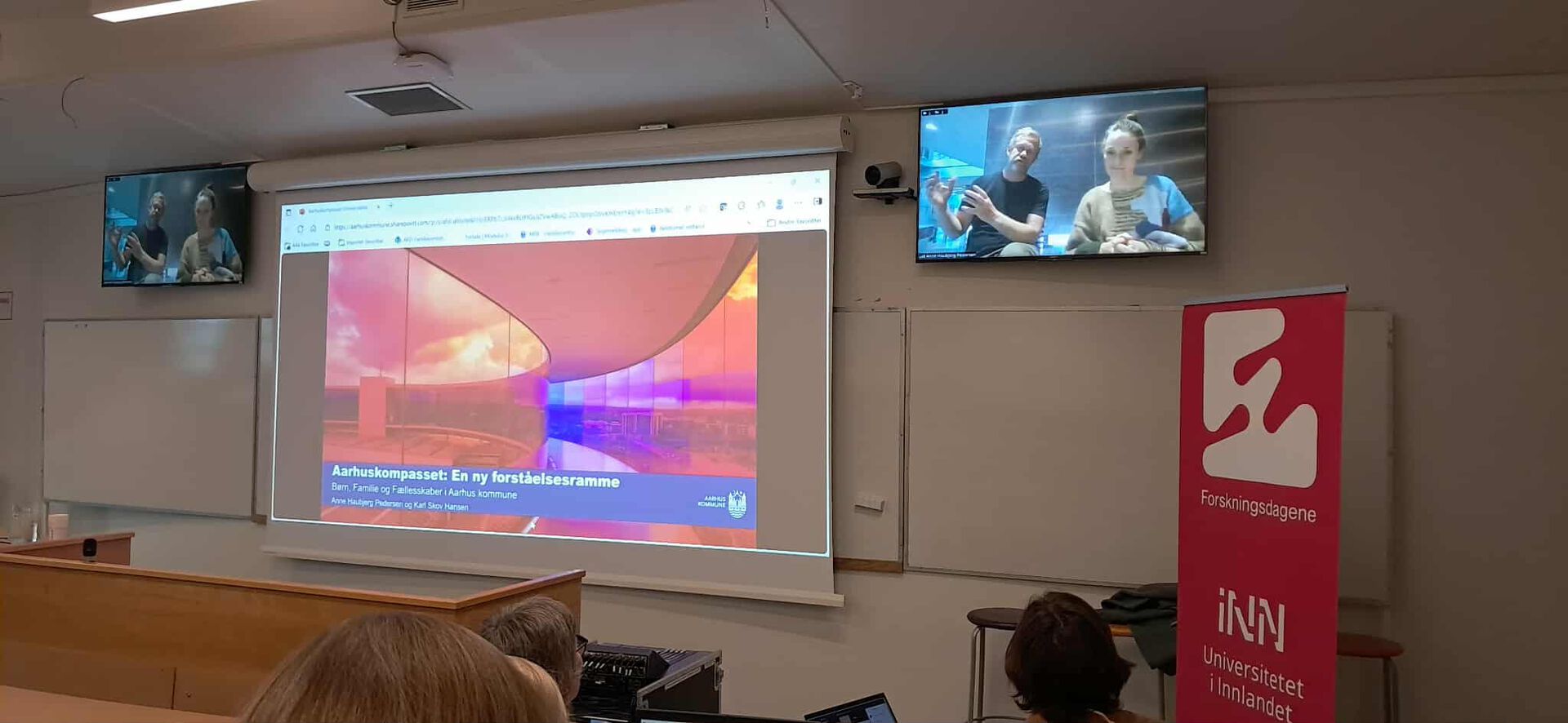 To personer med  på stream fra Danmark på en skjerm i et auditorium i LIllehammer