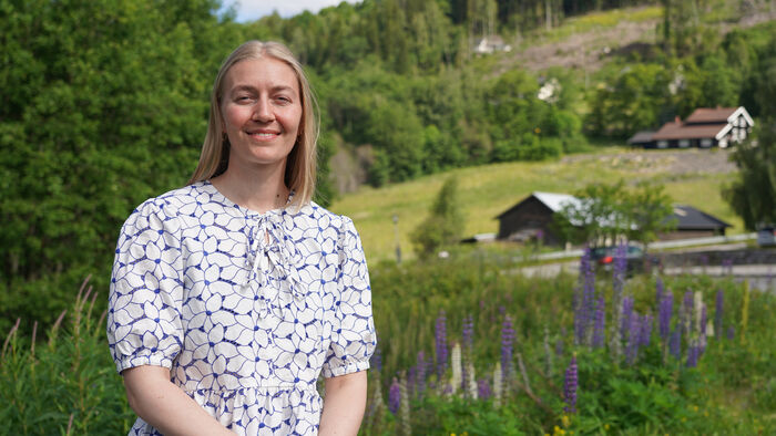 Ung dame med hvit bluse uten i sola foran noen trær