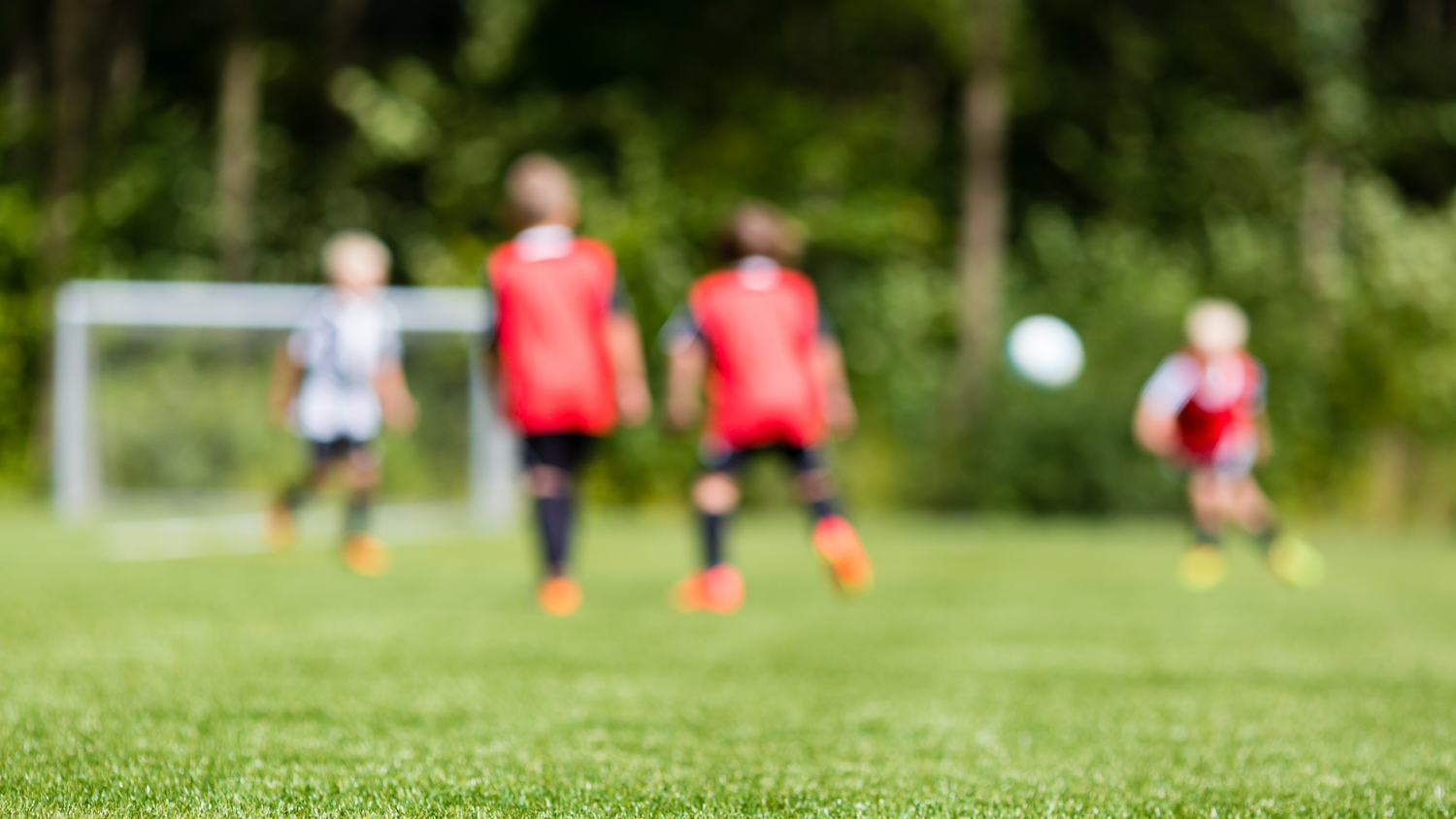Et uskarpt bilde av tre ungdommer som spiller fotball på en grønn gressbane