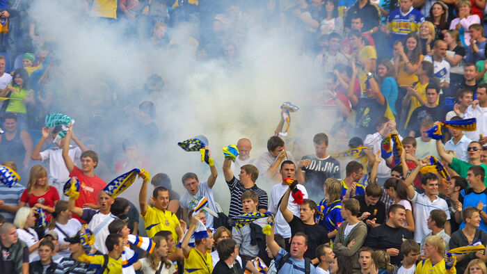 Engasjerte og ropende supportere på en fotballkamp med bluss og flagg