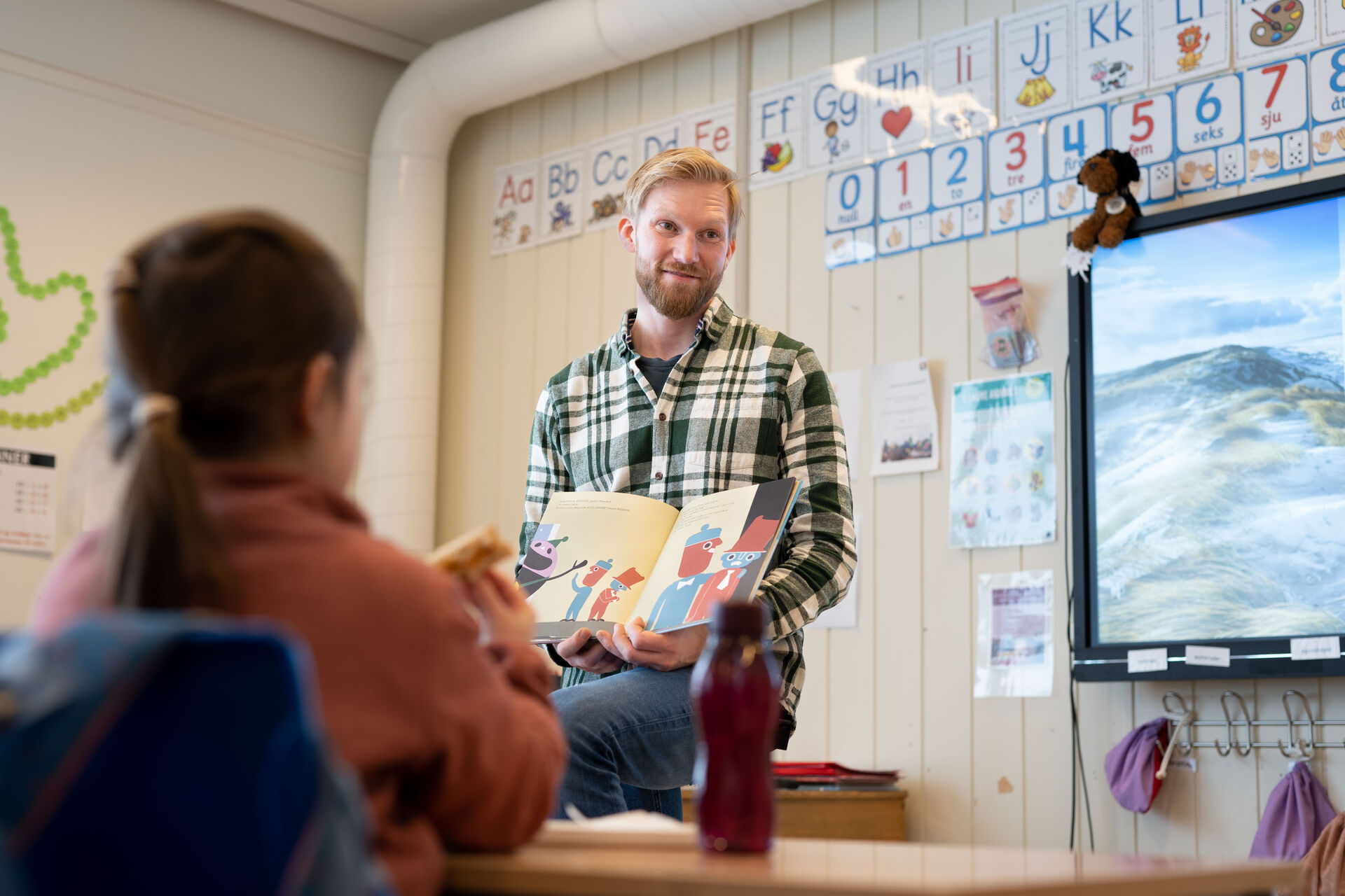 Halvor leser og viser frem en bok mens barna spiser.