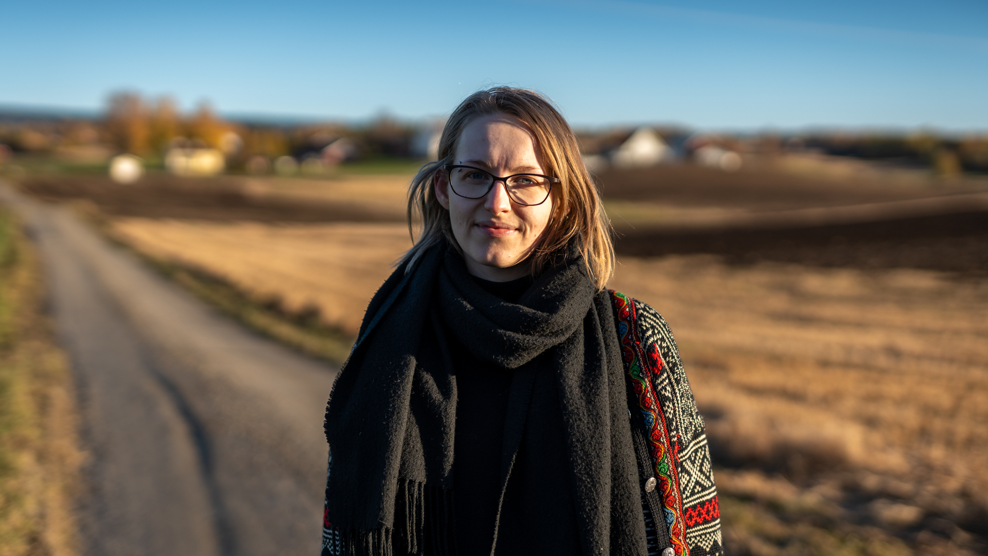 Portrettfoto av Elisabeth Egelid med åker og vei i bakgrunnen.