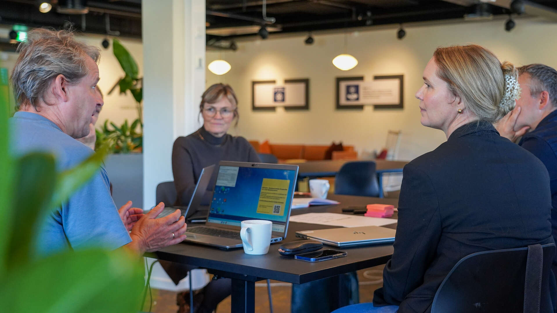 Fire personer sitter rundt et rundt bord og diskuterer