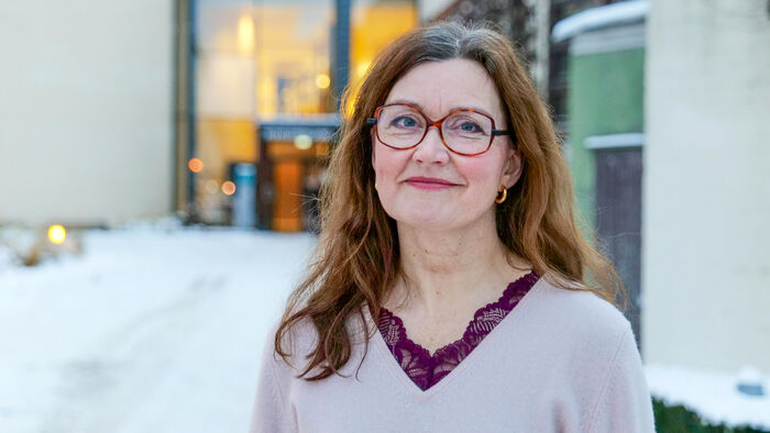 Dame med briller og lys lilla v-genser utenfor et bygg med snø på bakken
