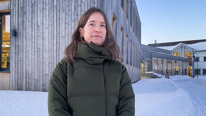 Hanne K. Sjølie utenfor campus Evenstad - et stort gråaktig trehus med ubehandlet panel og store vinduer