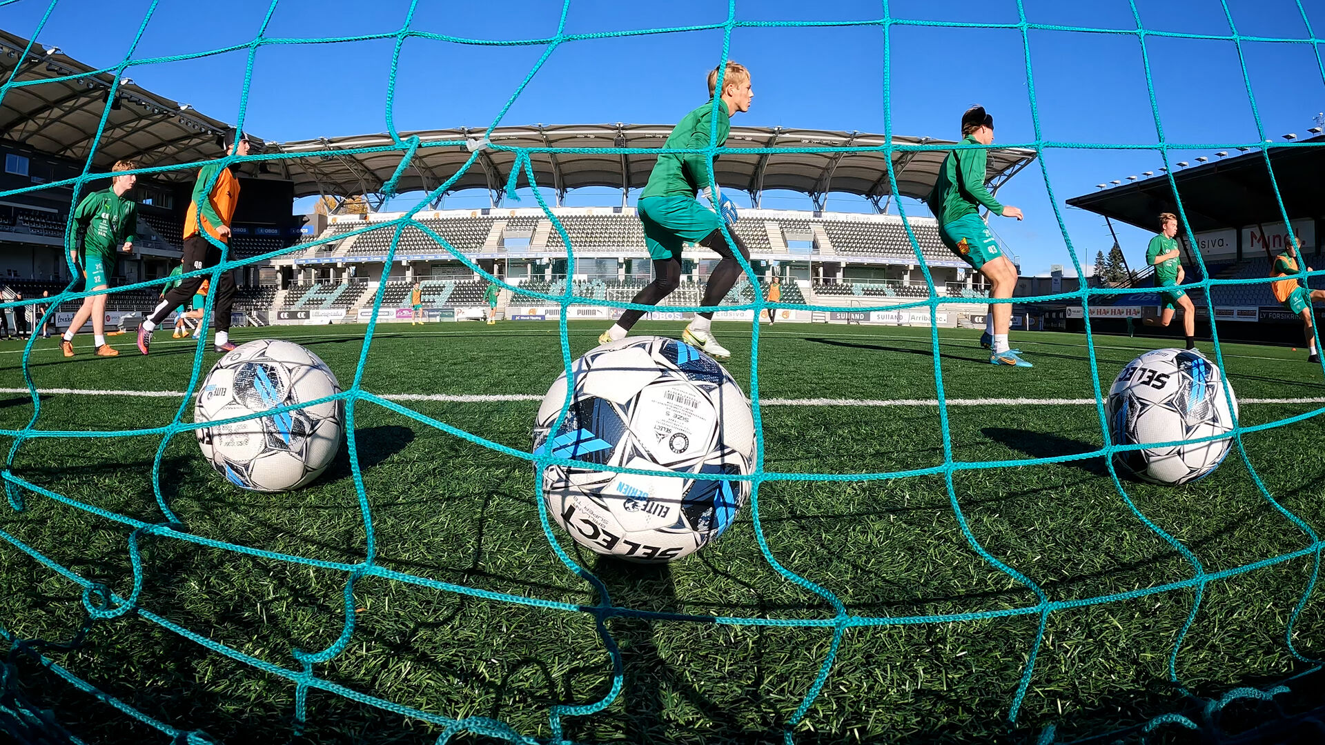 Fotballspillere som sparker ballene sine i mål - sett bak nettet.