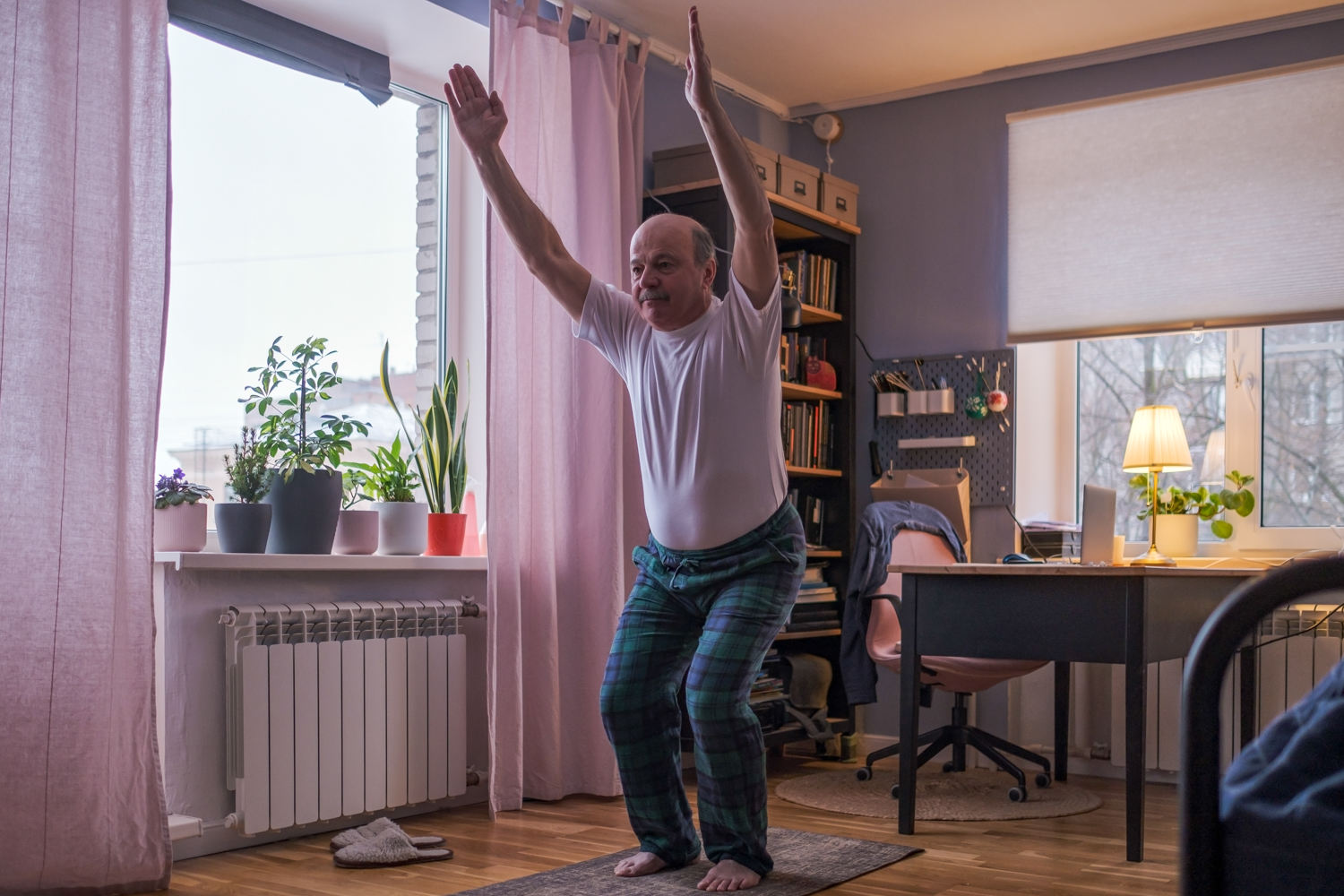 Gammel mann trener i egen stue med knebøy