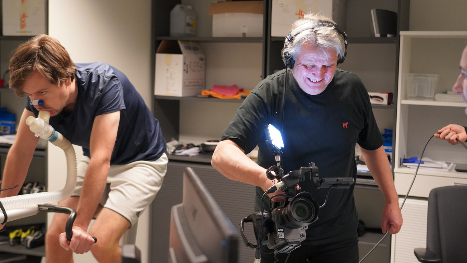 Mann på spinningsykkel mot speil mens mann filmer han