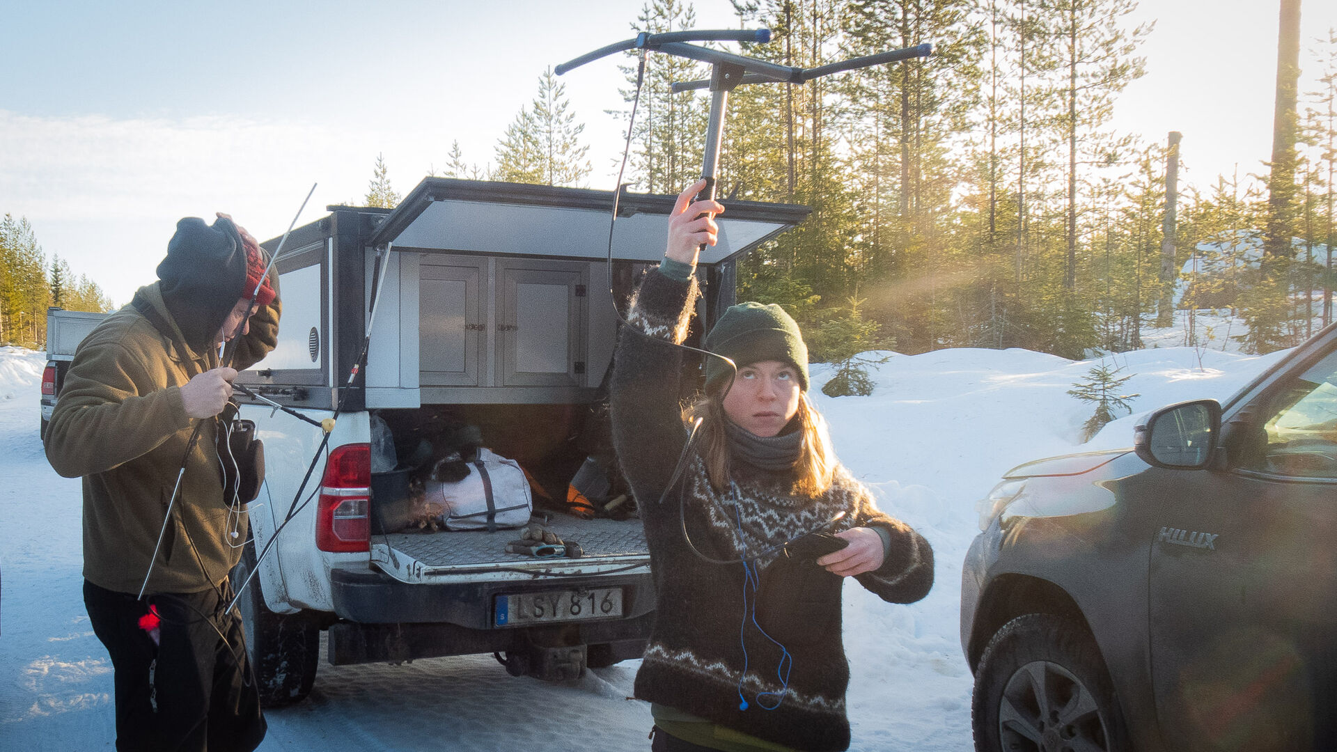 Researcher holding measuring equipment in the air in front of one of the cars with an open trunk.