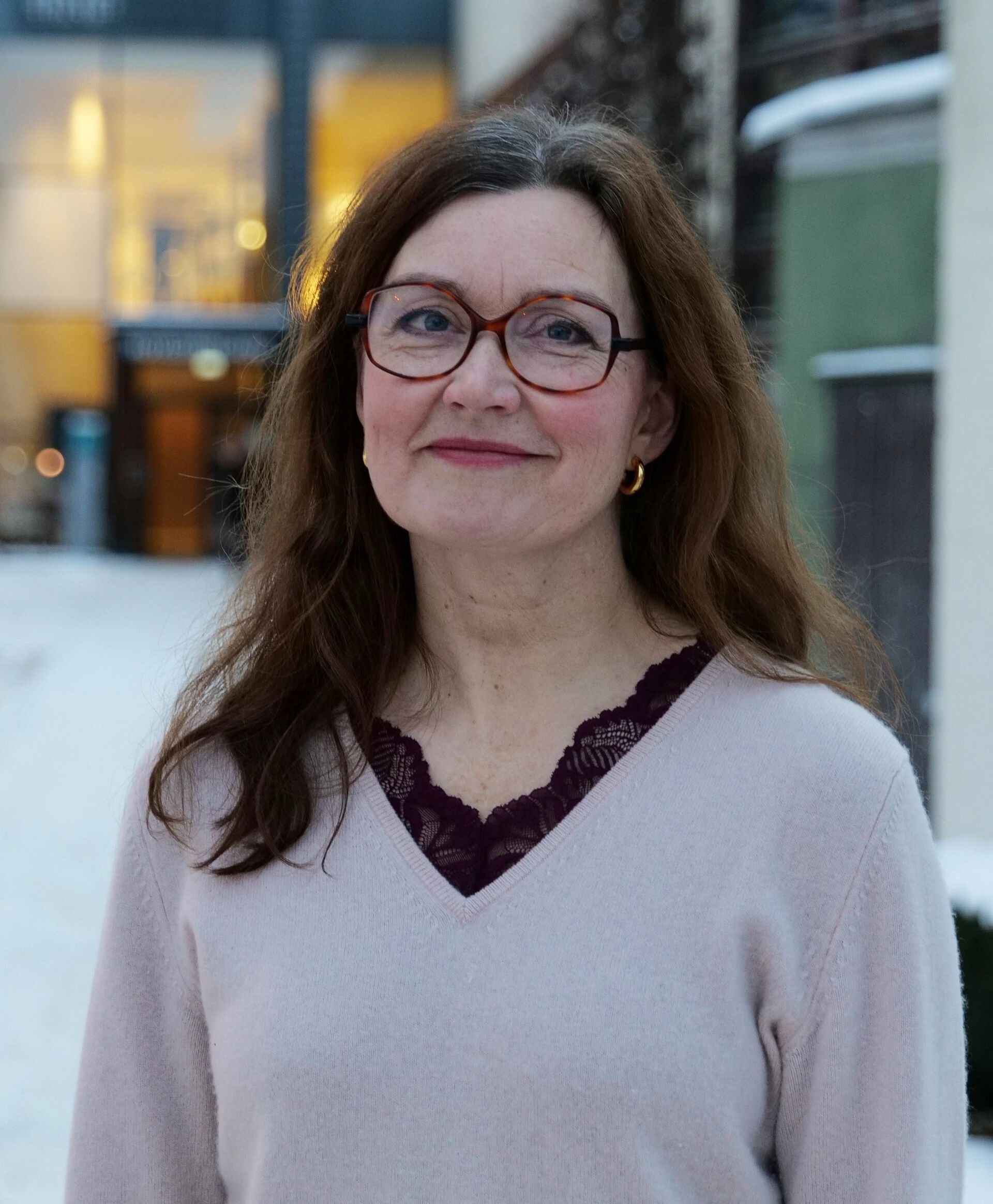 Portrettbilde av dame med briller ute foran et bygg med store vinduer