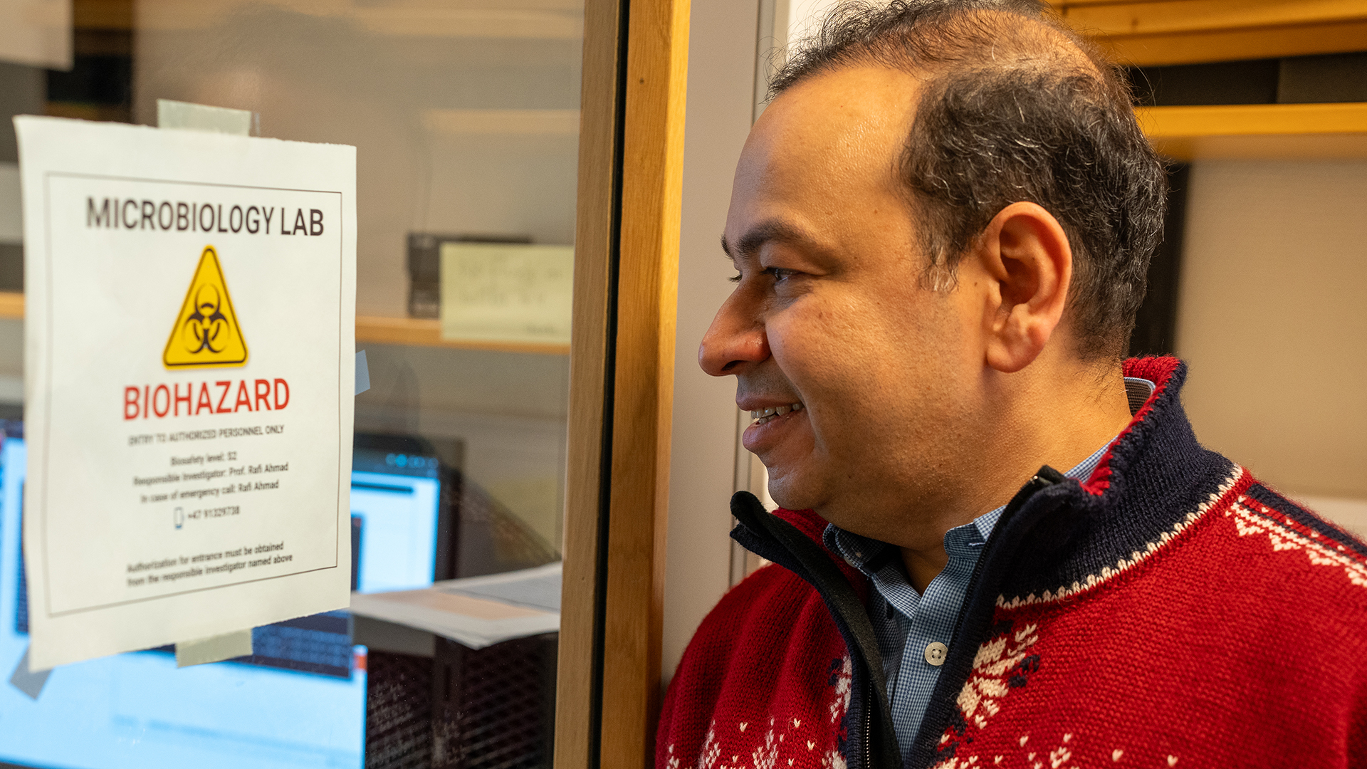 Rafi ser på døren inn til laboratoriet, der det står en plakat med advarsel om biologisk fare.