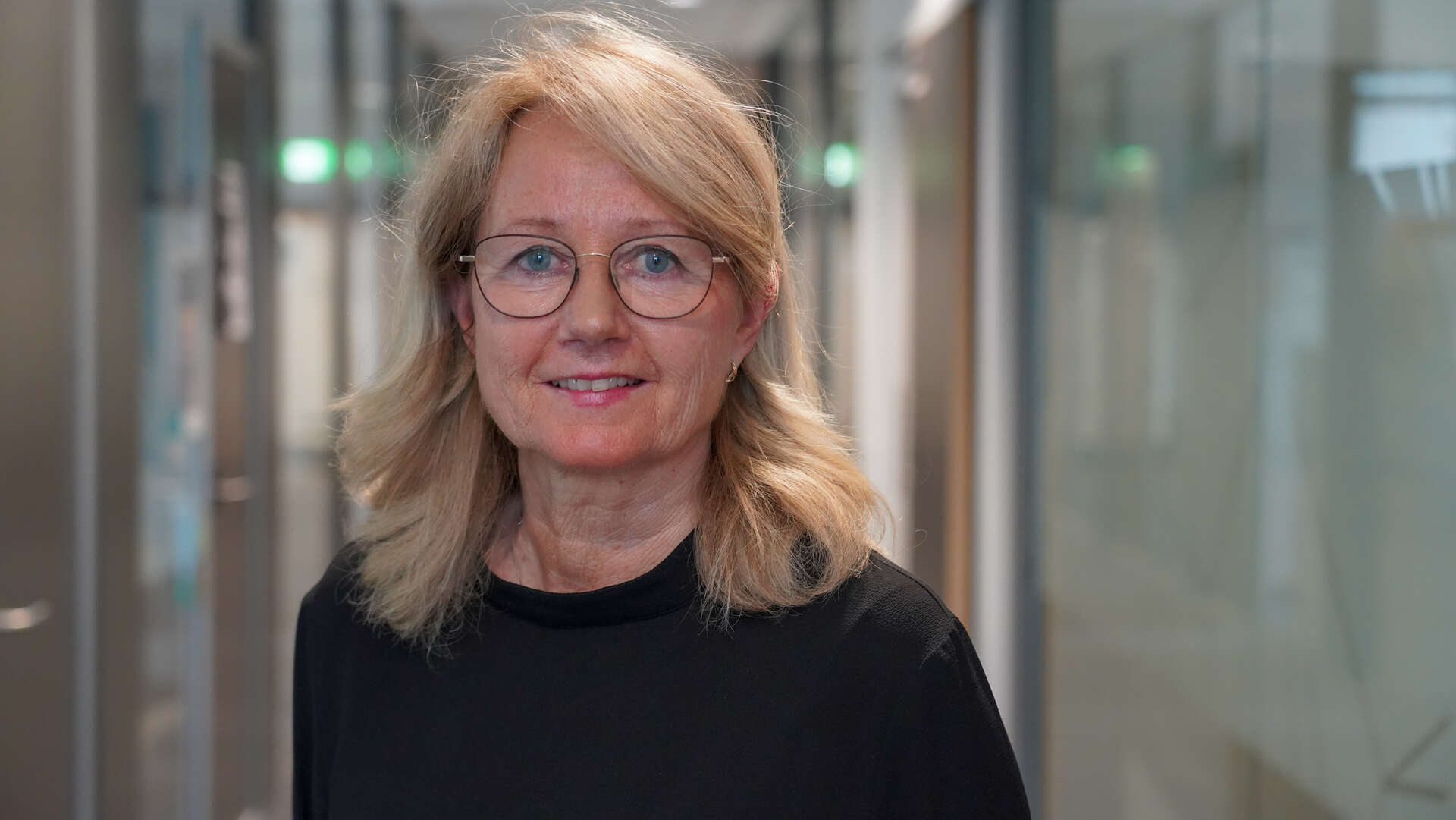 Dame med briller inne i en gang med glassdører
